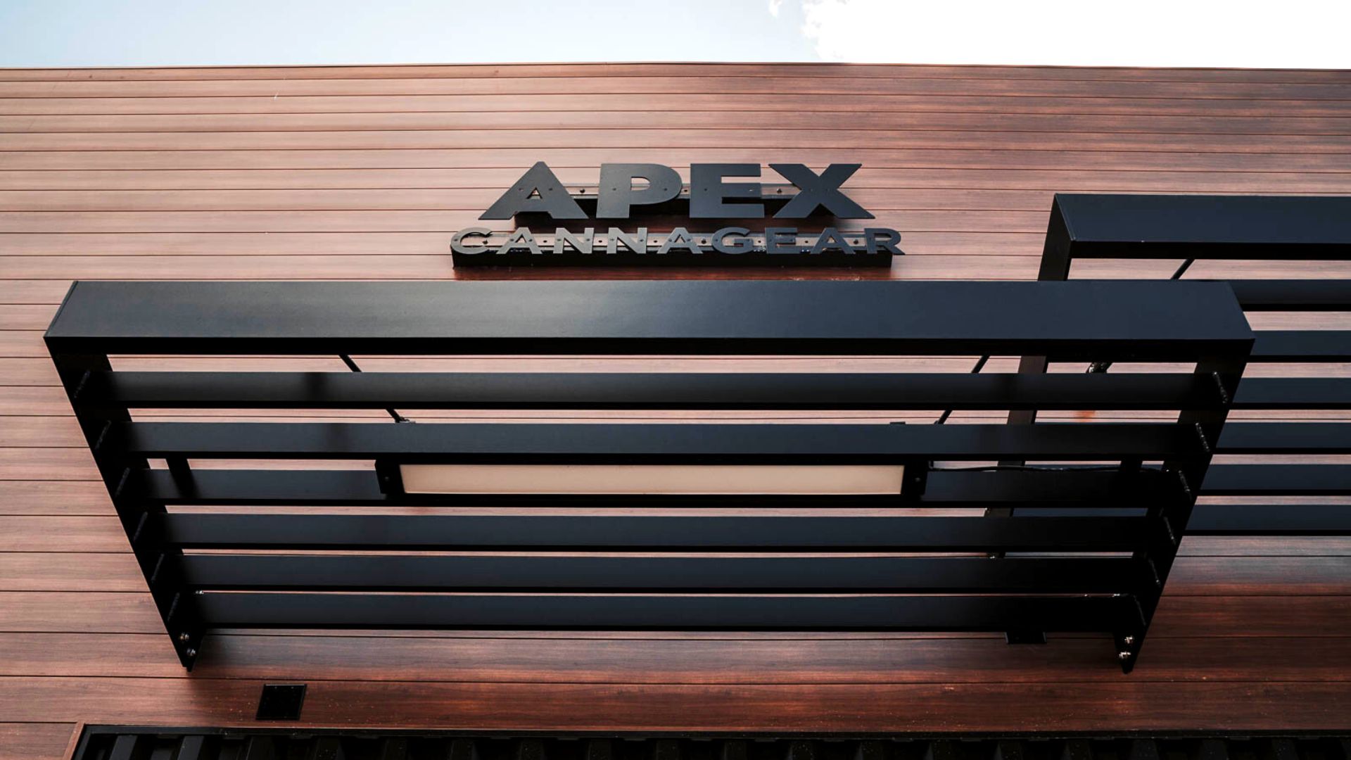 The image shows horizontal metal panels on the APEX building façade with the APEX sign mounted on the exterior architectural system.