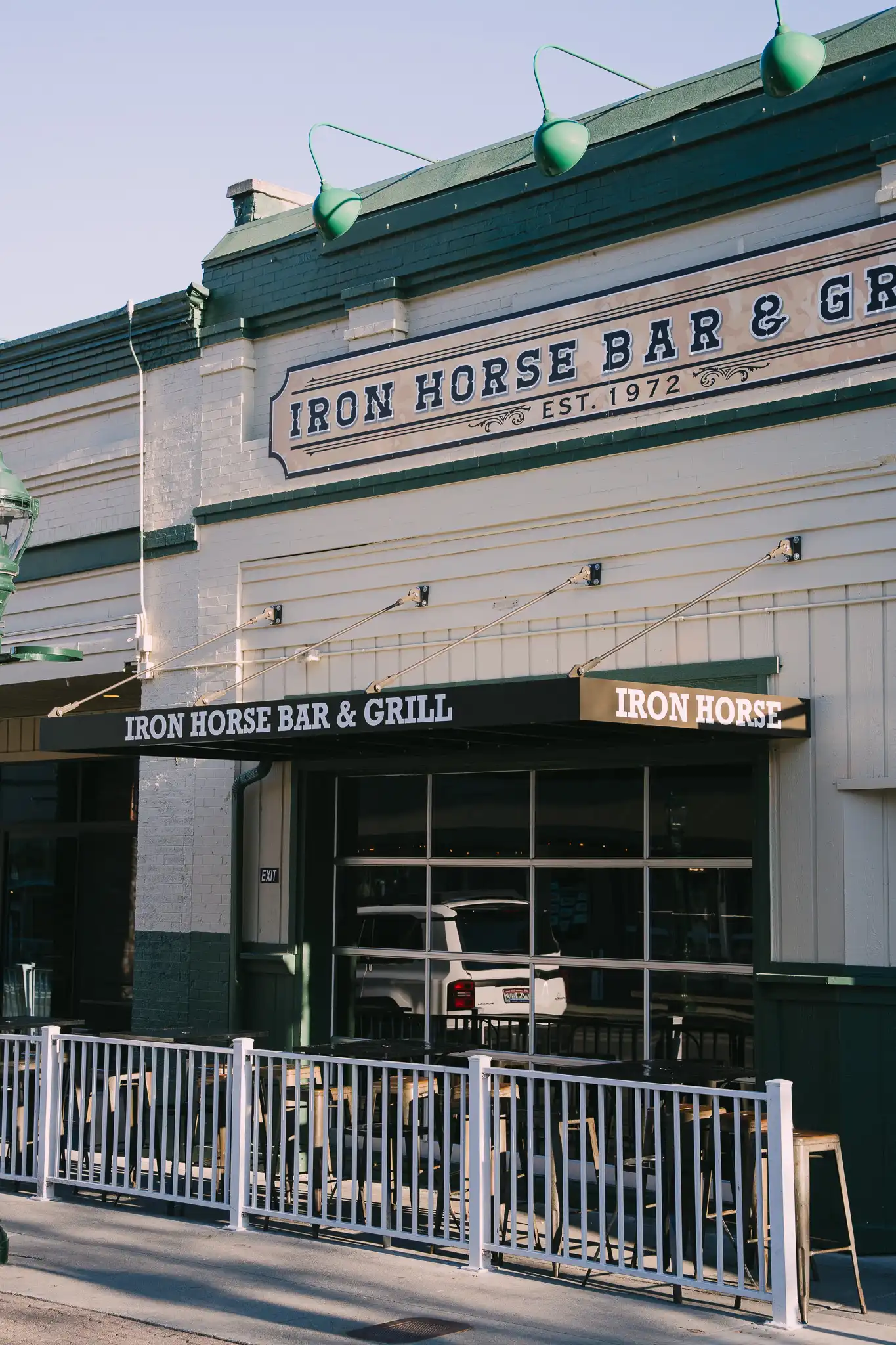 The image shows Iron Horse Bar & Grill with a black aluminum awning from Vestis extending over the storefront, covering outdoor seating and the main entrance.