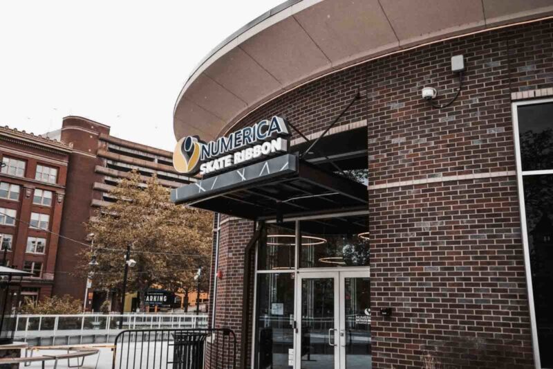 Numerica Skate Ribbon Public Space Architectural Canopy System The image shows a public recreation building entrance with a Vestis black architectural canopy extending over the Numerica Skate Ribbon signage and walkway.