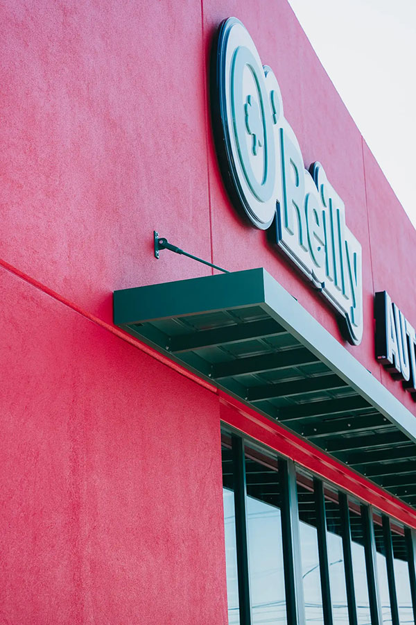 The image shows a close-up angled view of a Vestis aluminum canopy installed on an O’Reilly Auto Parts building, highlighting the underside and mounting brackets.