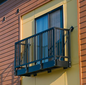 Vestis Aluminum Balconies The image shows a Vestis prefabricated aluminum balcony installed on a residential building with vertical siding and dark metal railings.