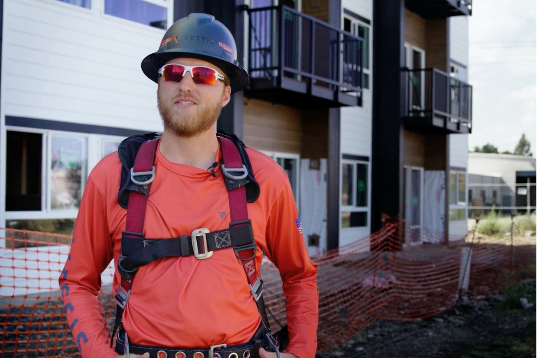 vestis team member standing in front of a commercial project with a hard hat and harness on smiling