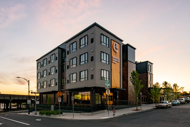 Schweitzer Haven Housing Architectural Canopy & Sunshade Systems The image shows a four-story multifamily housing building with Vestis architectural canopies and sunshade systems installed above the entry and window lines.